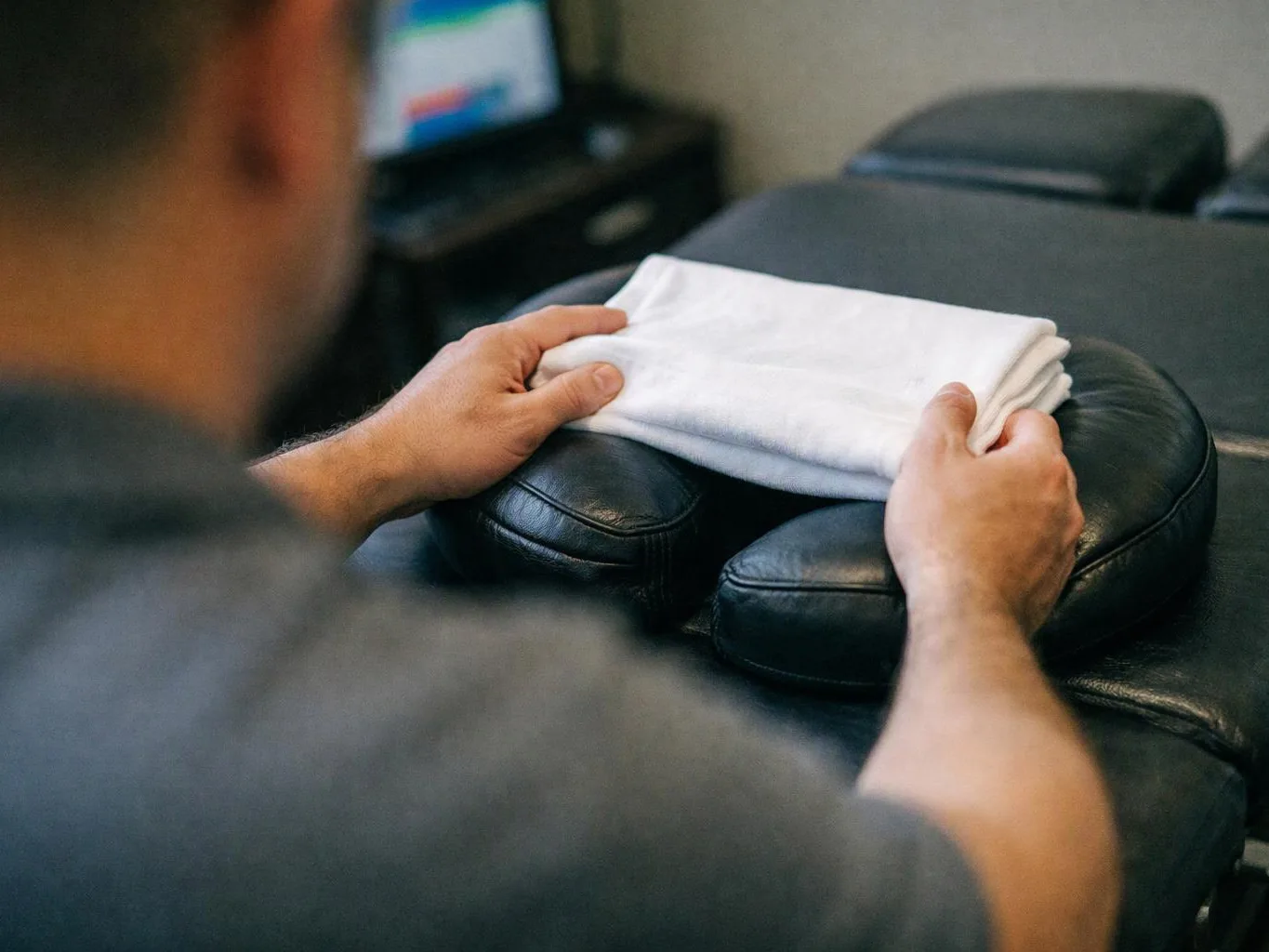 A person folds a white towel on a black padded massage table in a quiet room