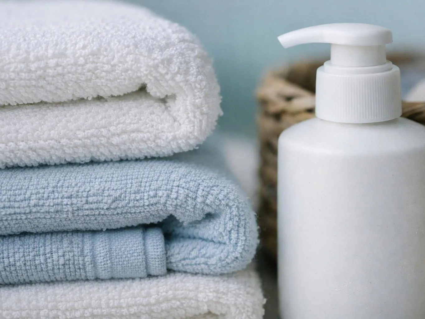 Stacked white and blue towels sit beside a white pump bottle on a soft bathroom surface